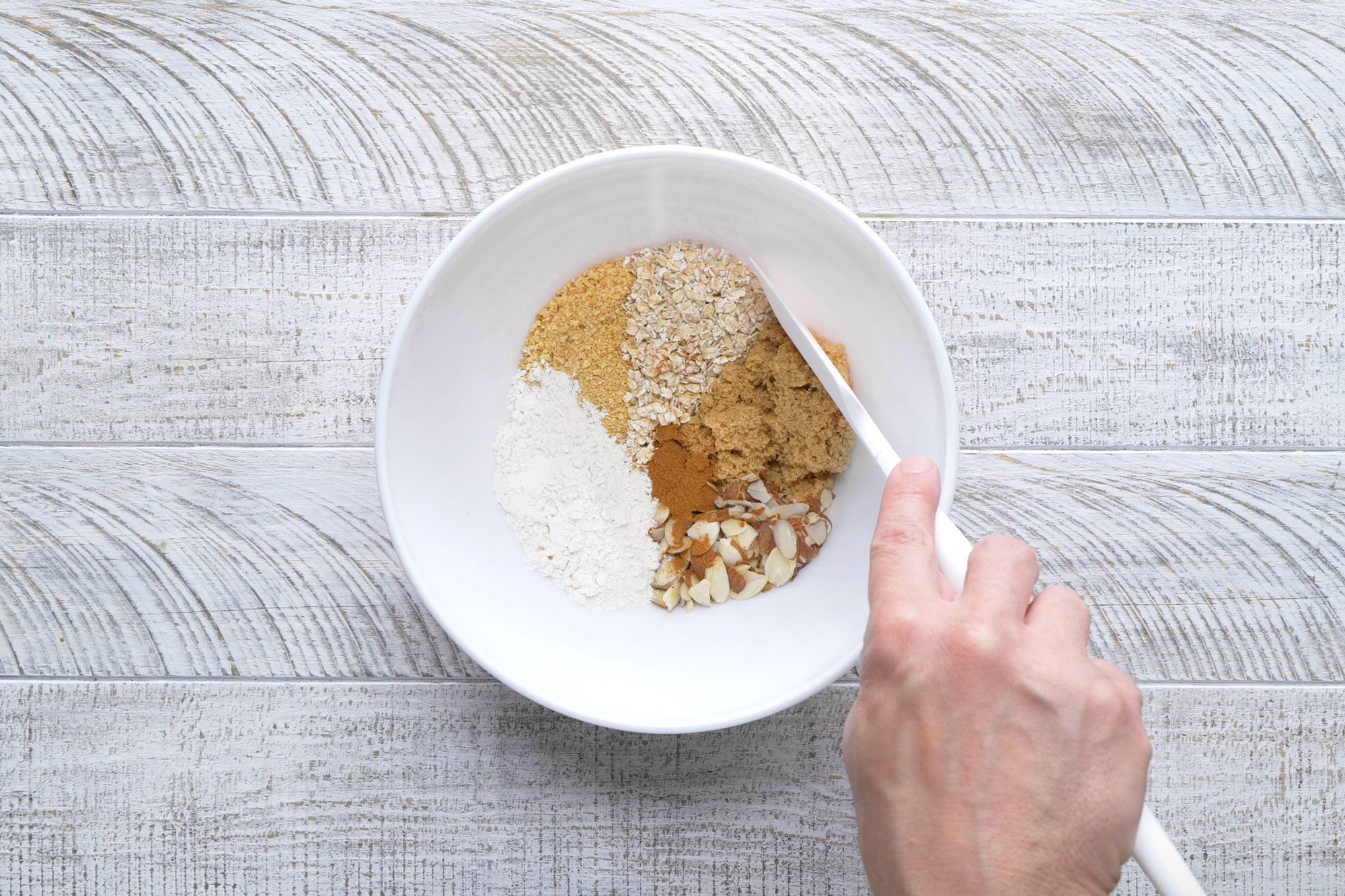 overhead shot; white textured background; In a small bowl, combining the cracker crumbs, oats, brown sugar, almonds, cinnamon and remaining flour;