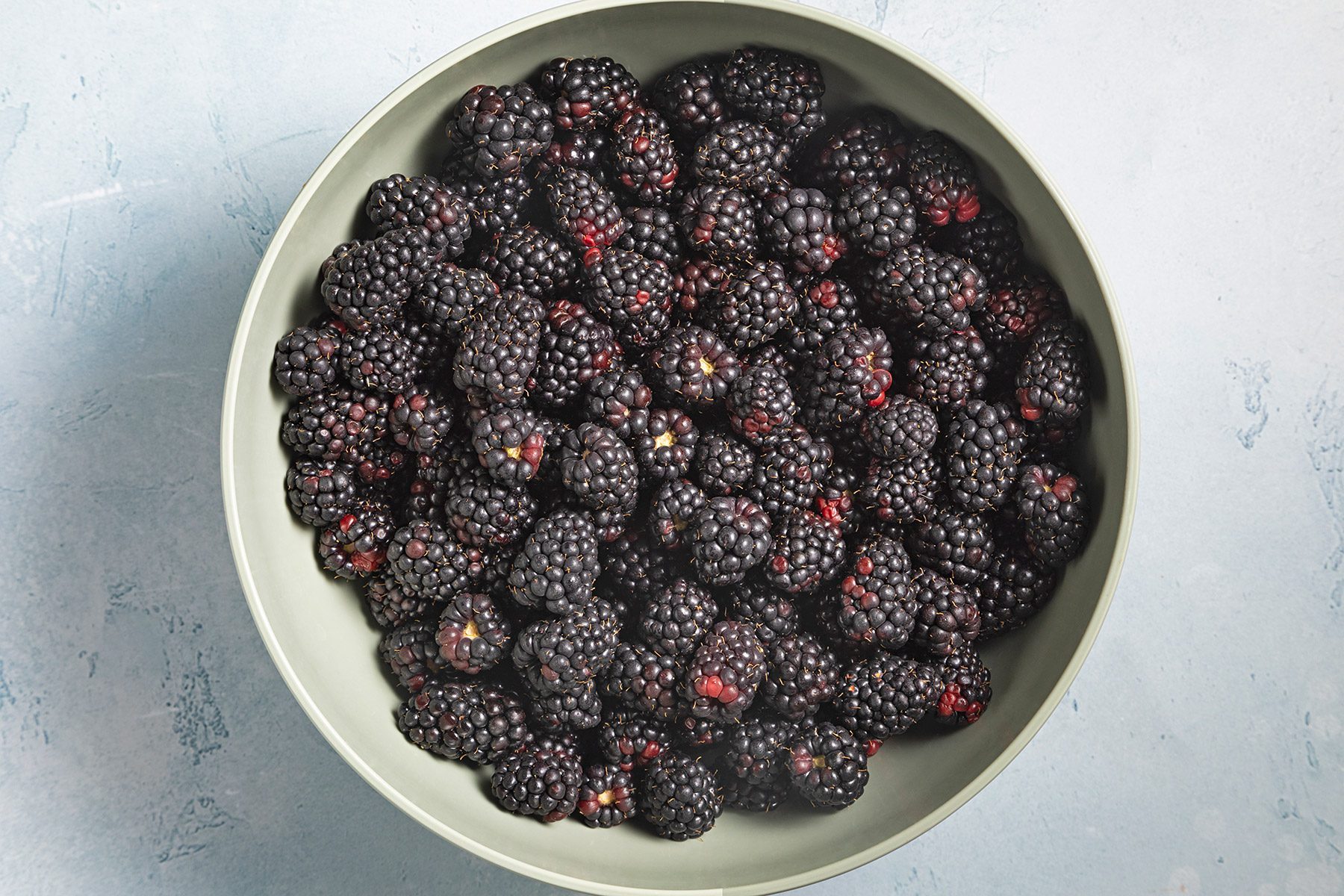 Overhead shot of blackberries in a large bowl; blue marble background