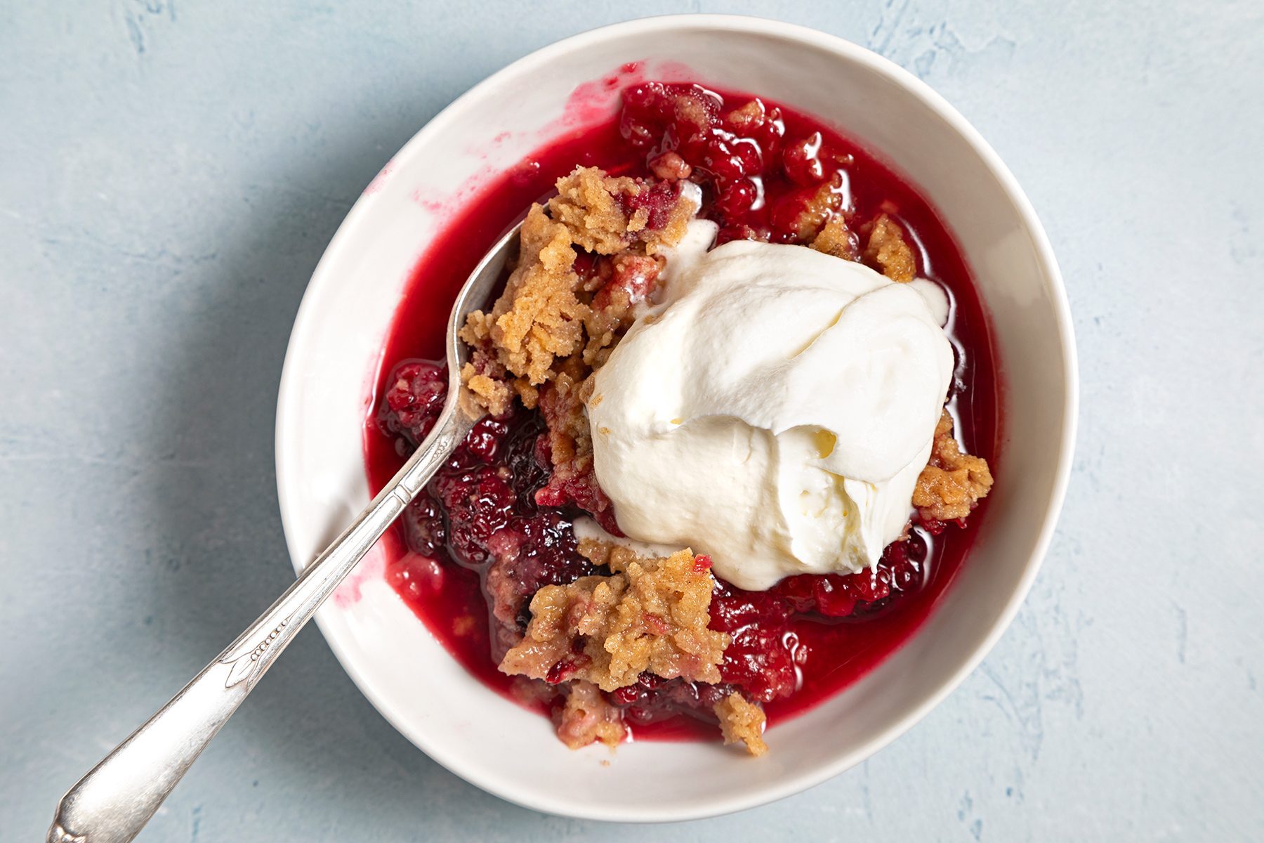 Overhead shot of Blackberry Crumble; served in bowl with ice cream; spoon; blue marble background