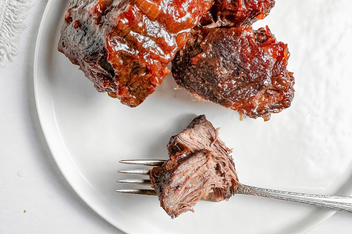 Taste of Home boneless beef short ribs on a white ceramic plate with a vintage silver fork next to a cloth napkin.