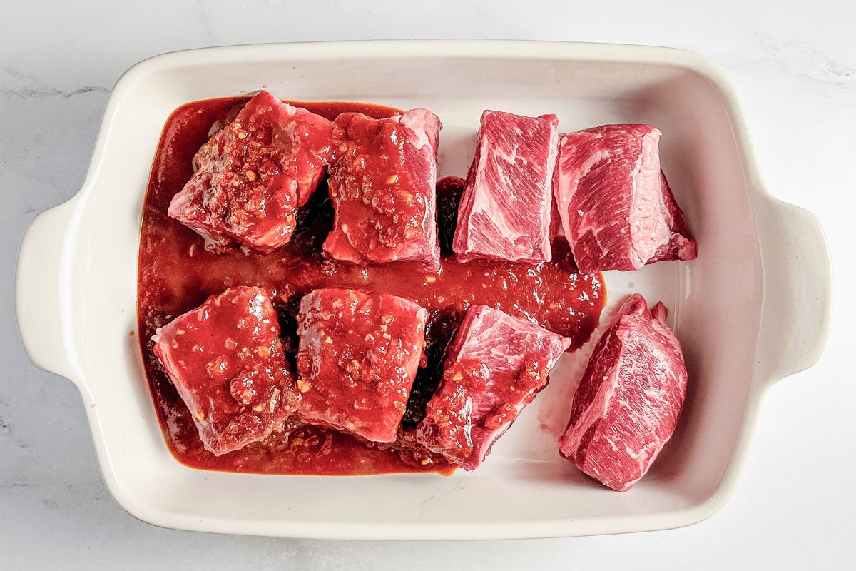 Uncooked Taste of Home boneless beef short ribs in a white ceramic baking dish on a marble surface.