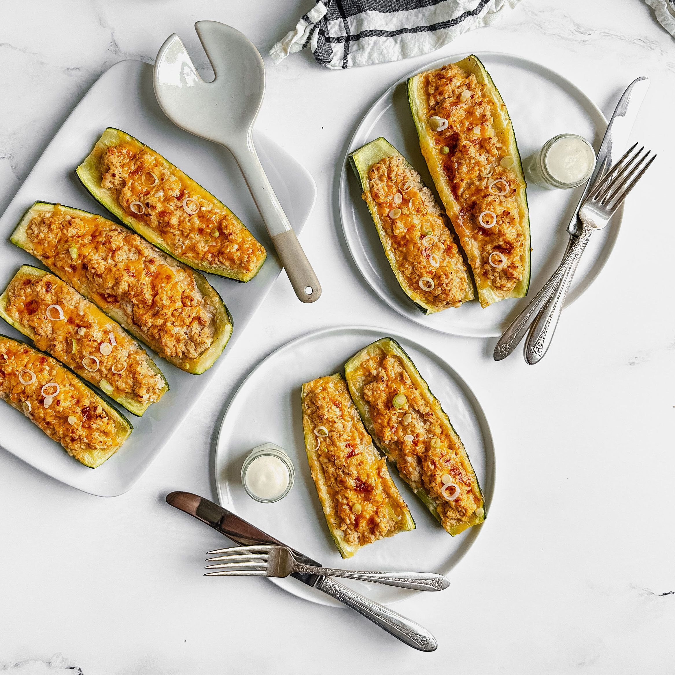 Taste of Home Buffalo Chicken Zucchini Boats on white ceramic plates and tray next to a striped cotton napkin.