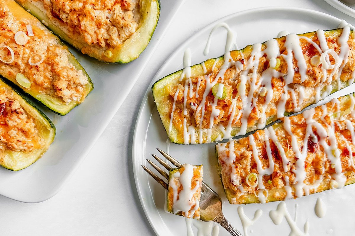 Taste of Home buffalo chicken zucchini boats drizzled with ranch dressing on white ceramic plates and tray