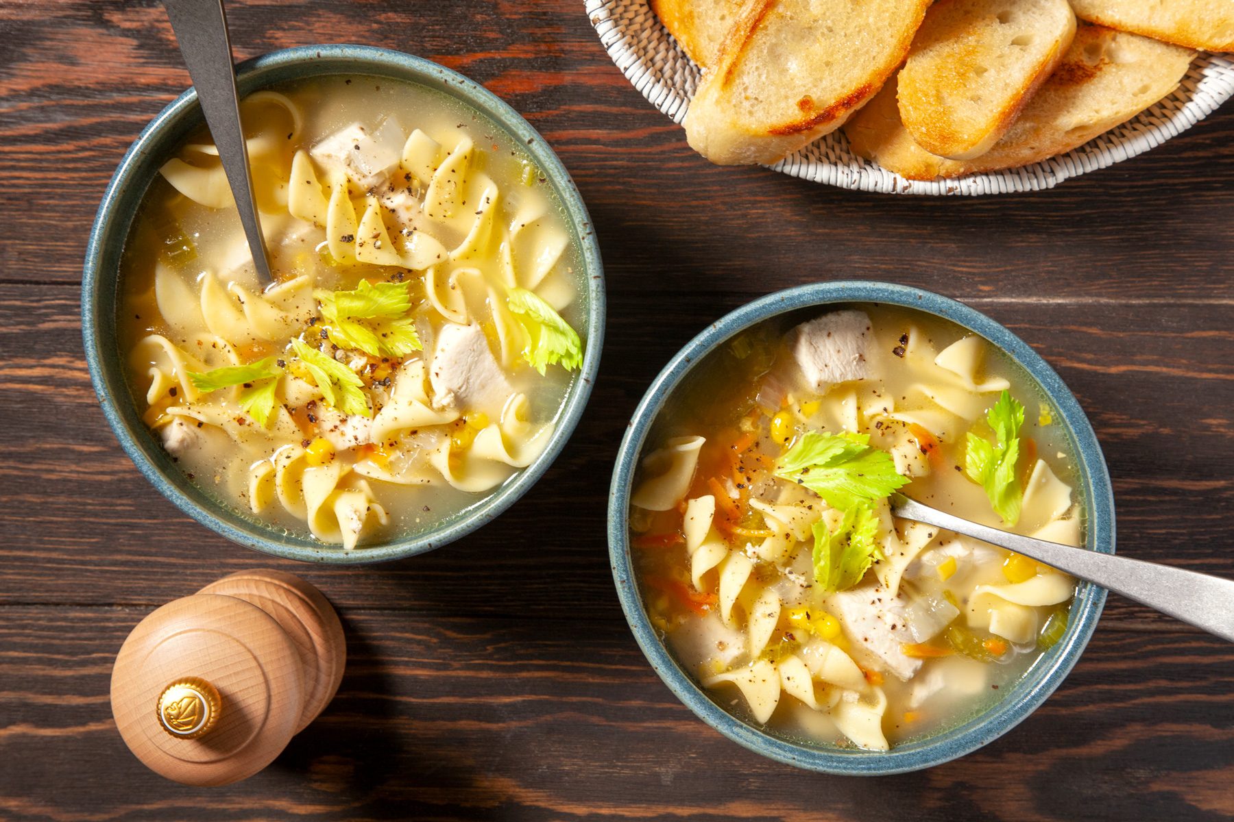 Two bowls of Chicken Corn Soup topped with celery leaves and cracked pepper