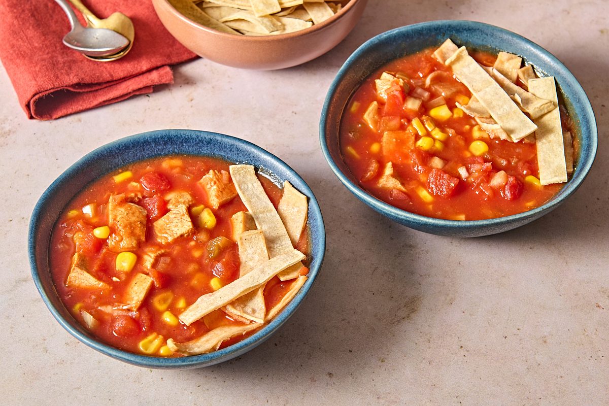 Chicken tomato soup ladled into two bowls and topped with tortilla strips