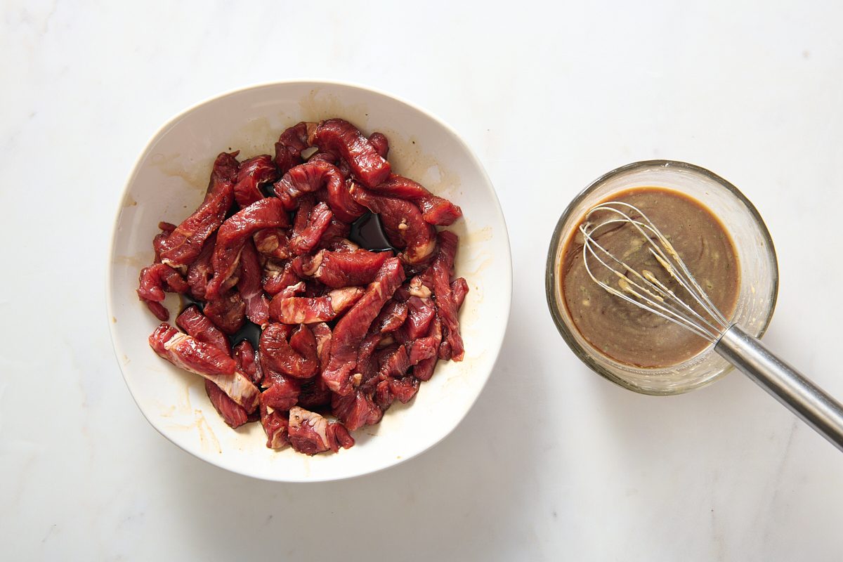 Steak being marinated in a shallow bowl with the whisked sauce in a separate bowl next to it