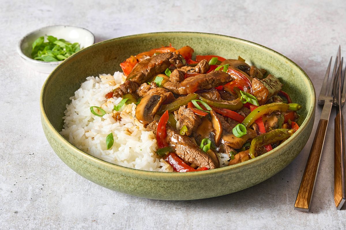 Angled image of Chinese pepper steak served with rice in a bowl plate