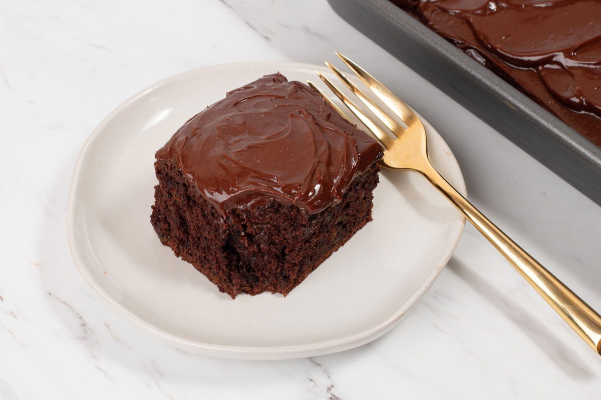 Chocolate Zucchini Cake portion on a plate with full tray nearby