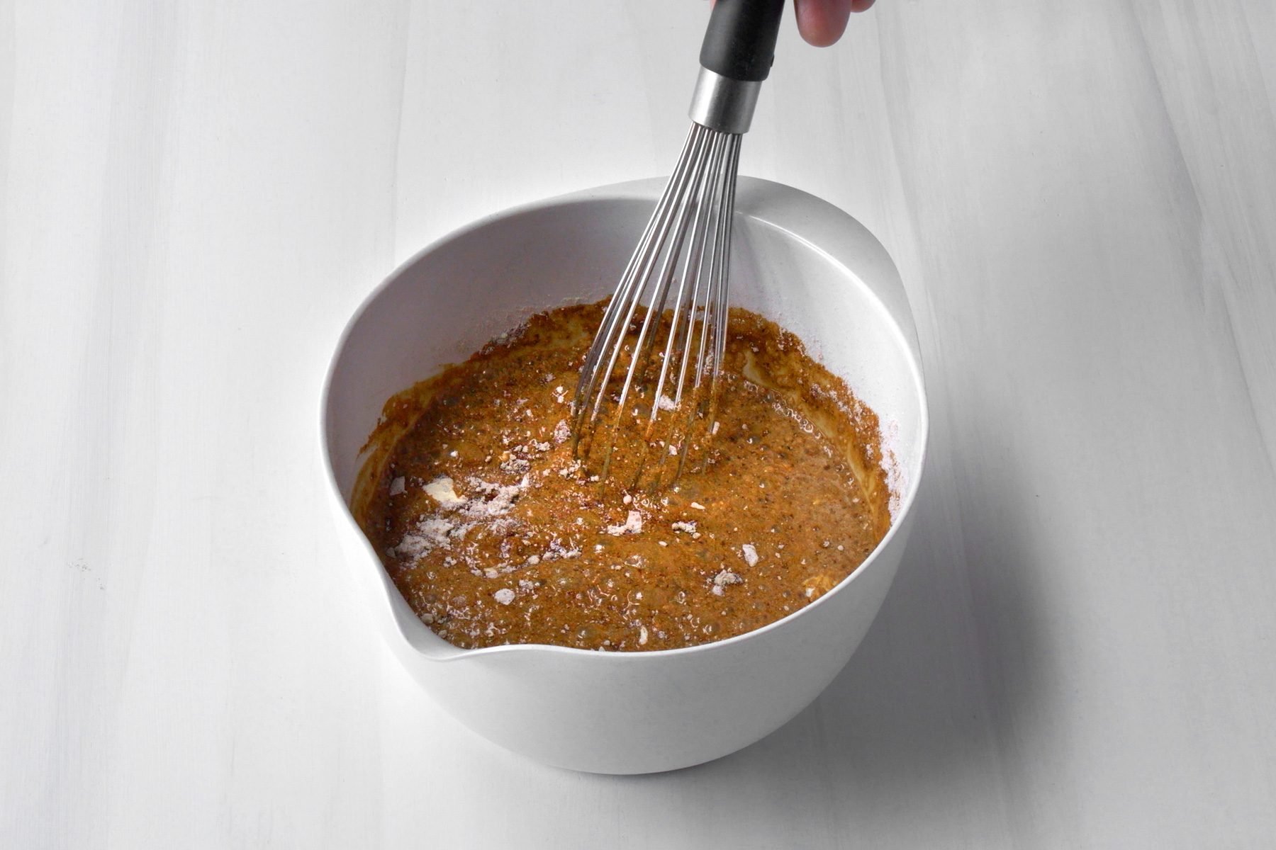 A hand whisking gravy in a white bowl