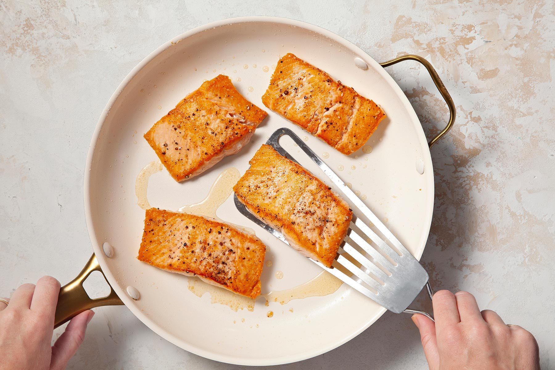 Overhead shot of large skillet; heat oil and add salmon; cook until salmon just begins to flake easily woth fork; flatter spatula; induction; cream marble background