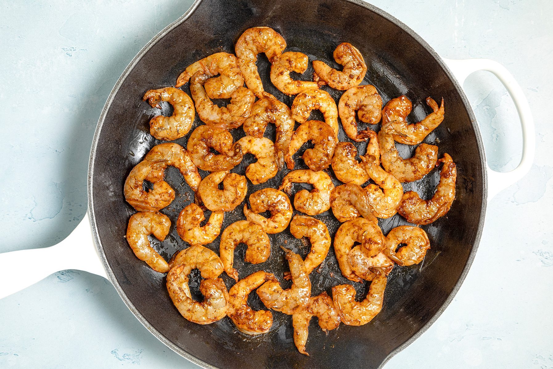 A cast iron skillet filled with cooked shrimp seasoned with spices. 