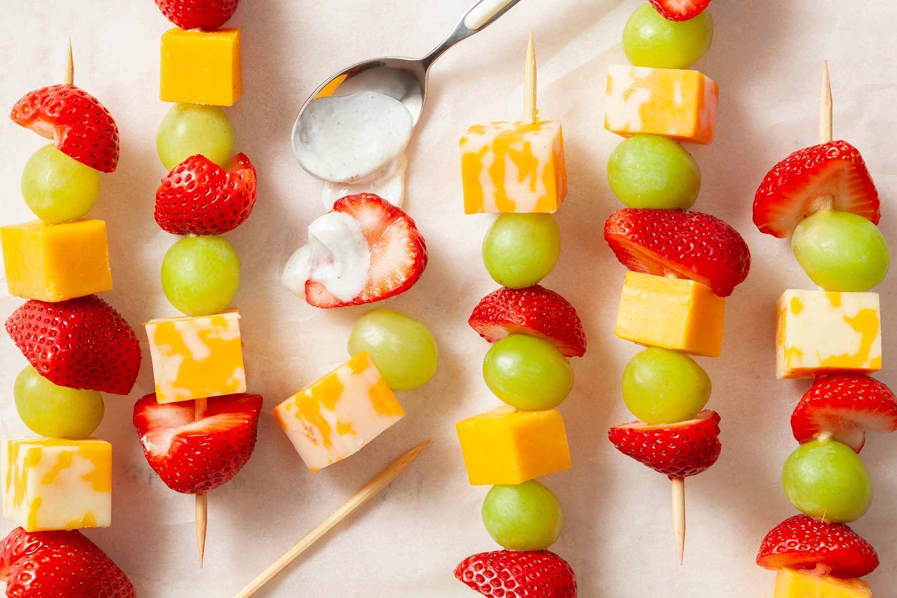 overhead shot; white background; Fruit & Cheese Kabobs on wooden skewers placed over background with silver spoon;