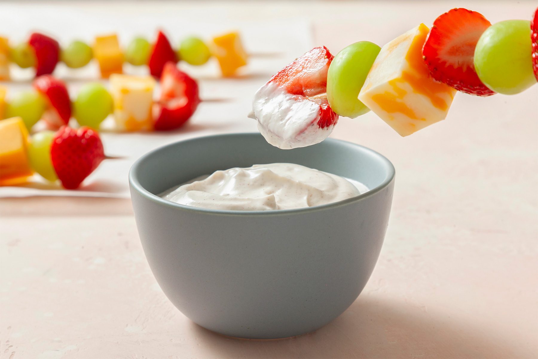 horizontal shot; white background; Fruit & Cheese Kabobs on wooden skewers dipped into cream from small bowl