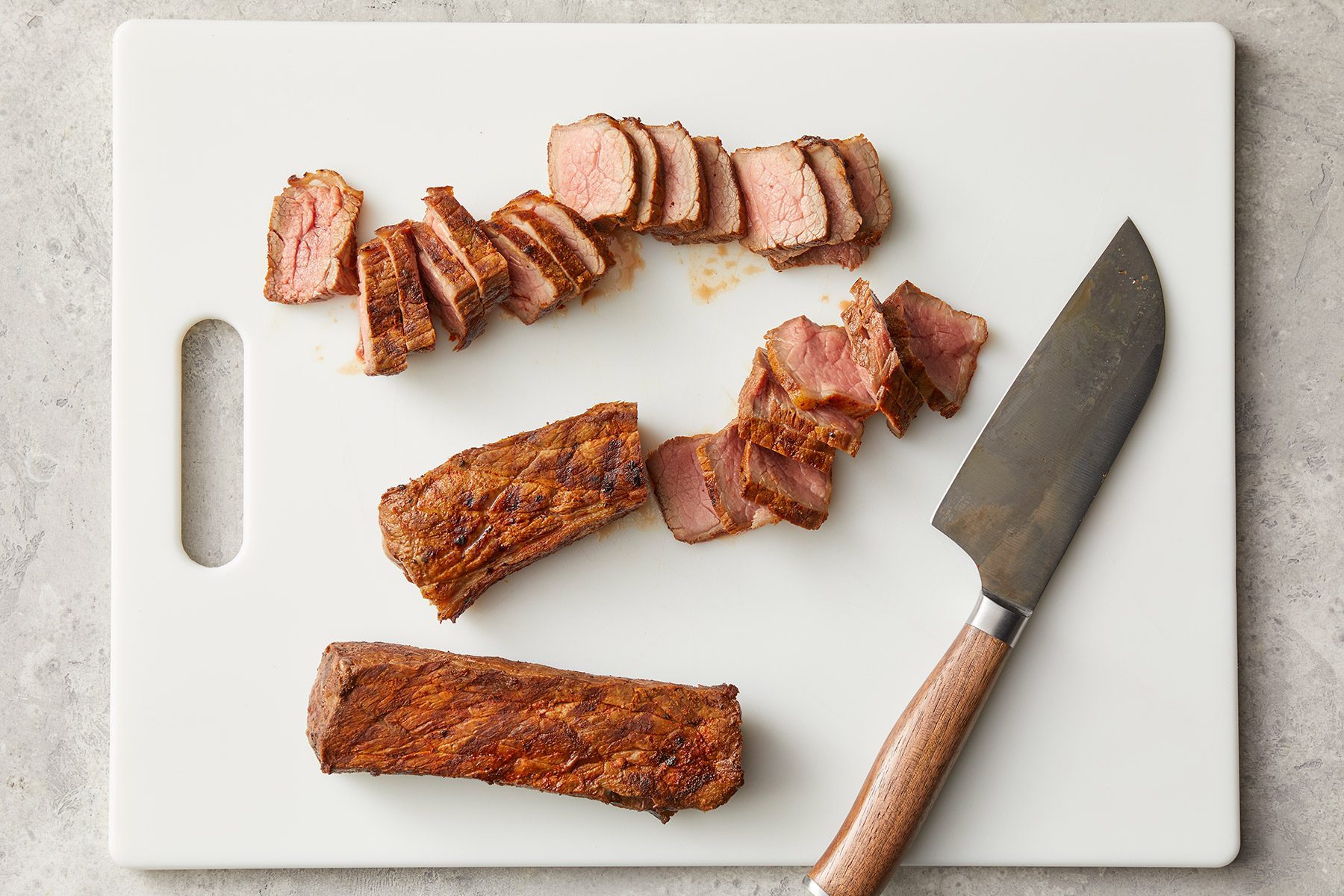 Overhead shot of grilled ribs; cut thinly slicing; knife; white chopping board; marble background
