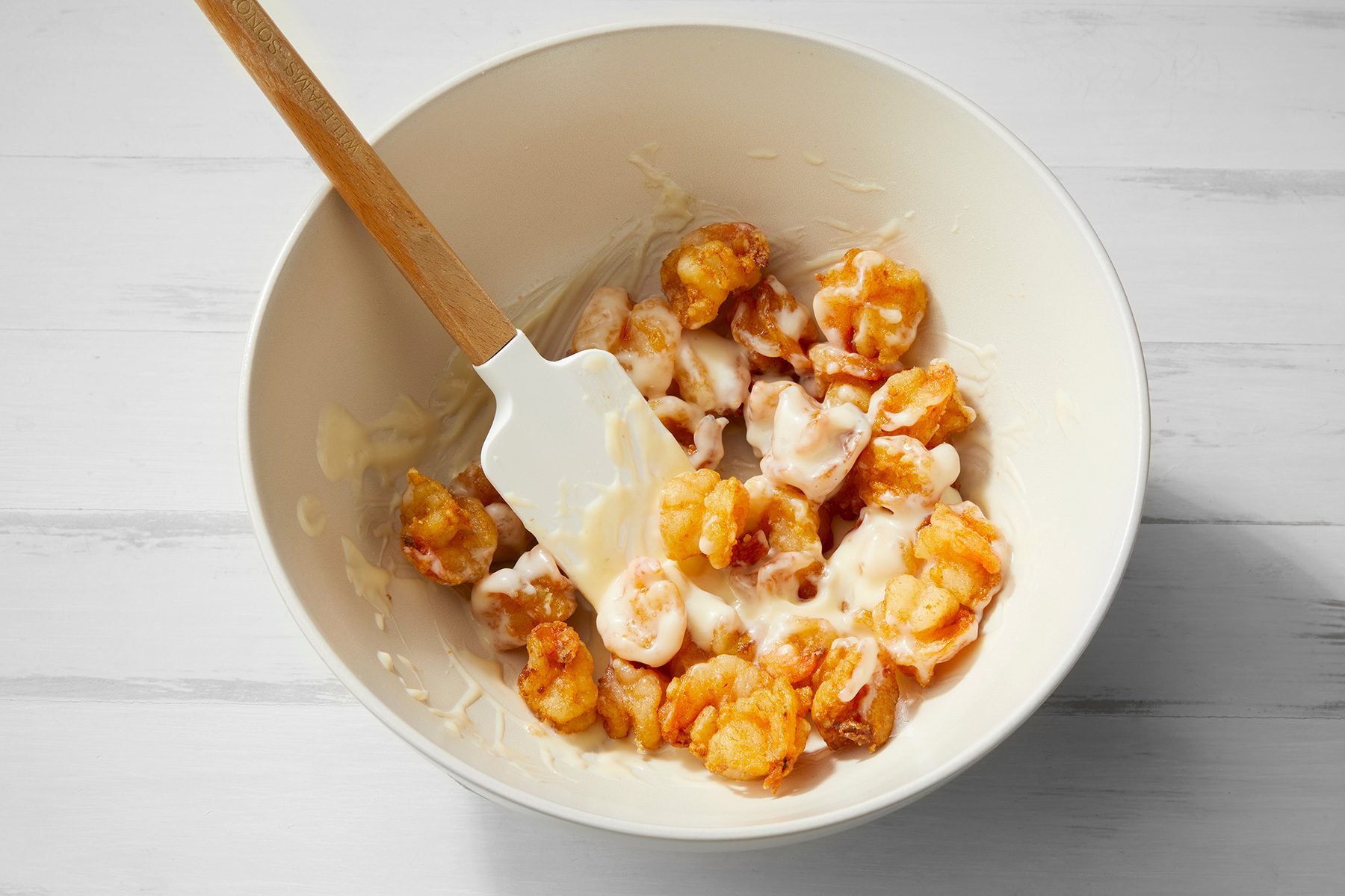 white background; Coating Shrimps into mixture in a large bowl using spatula;