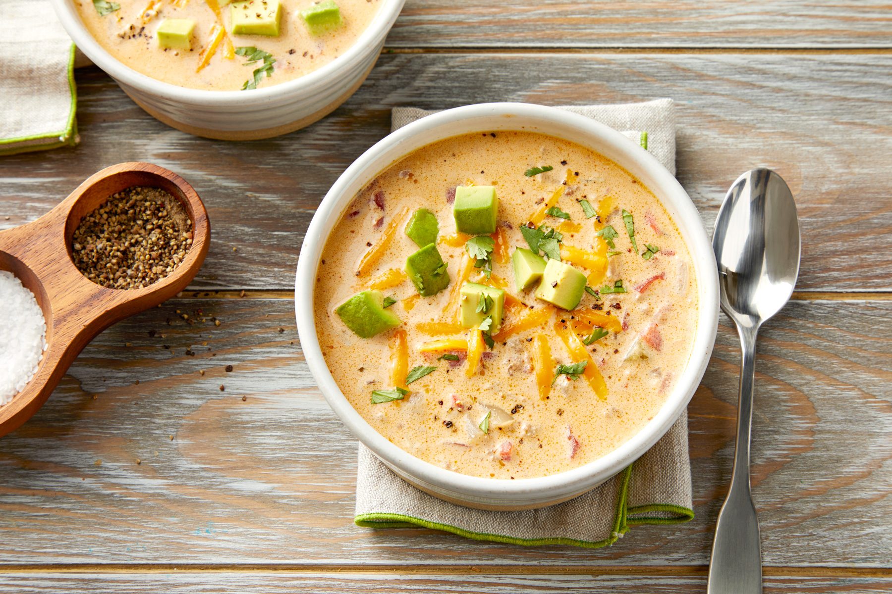 A bowl of Keto Taco Soup garnished with shredded cheddar cheese and sliced avocado