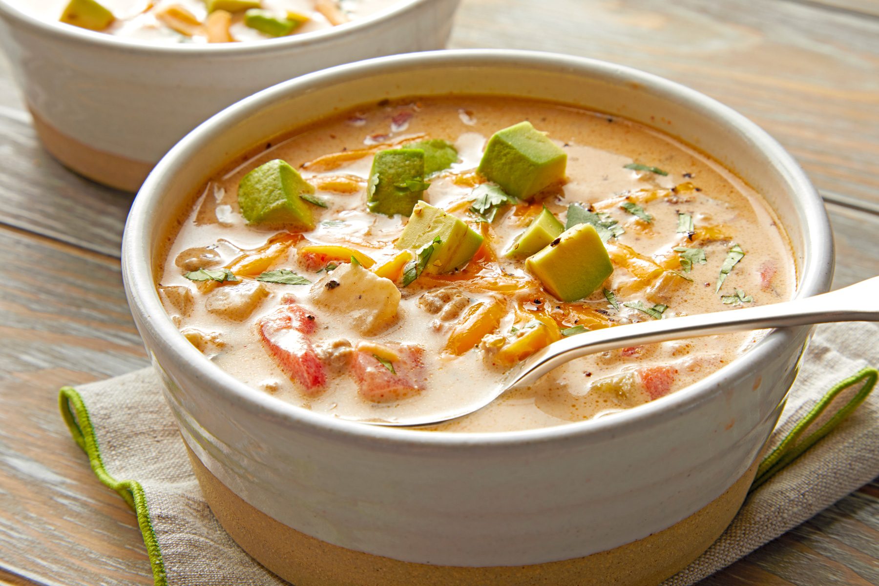 A bowl of Keto Taco Soup garnished with shredded cheddar cheese and sliced avocado