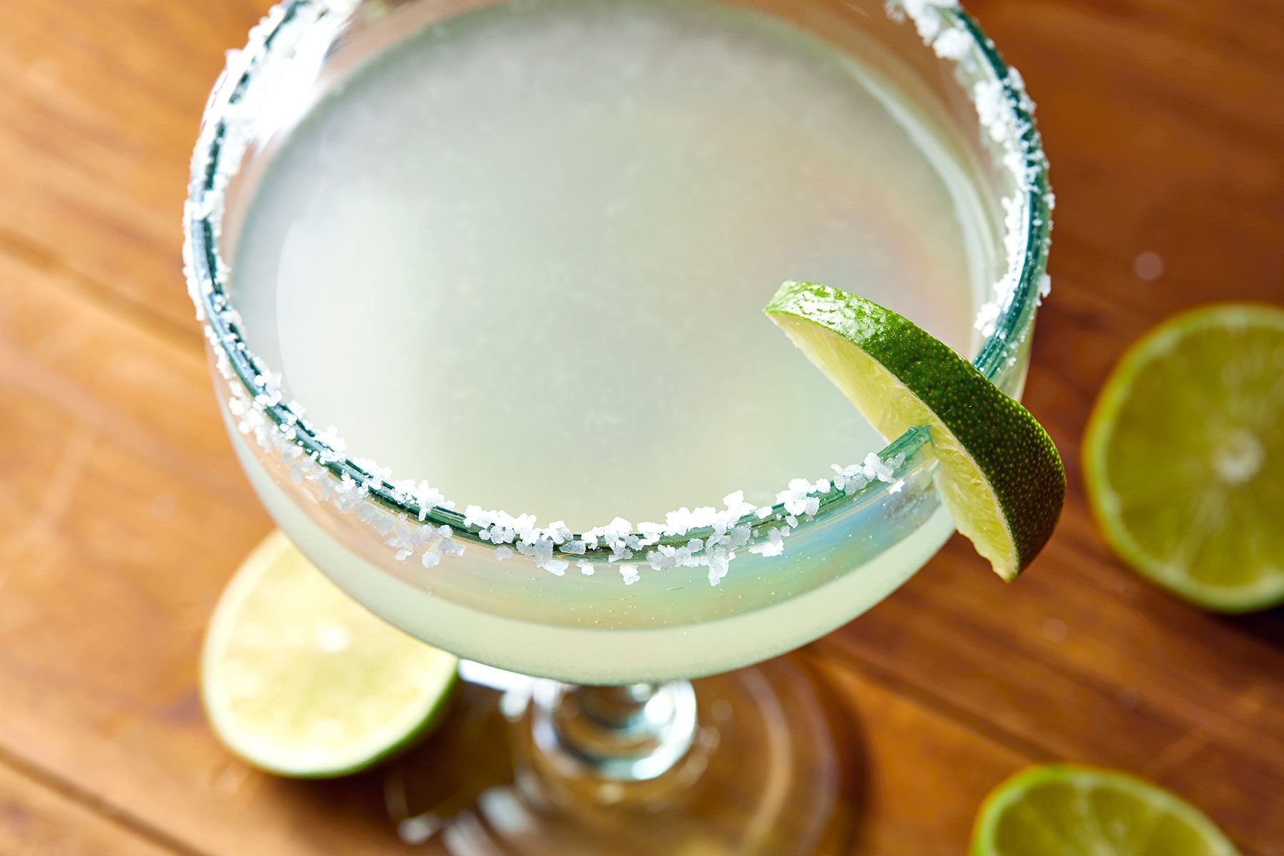 Close shot of Mezcal Margarita; in glass garnished with lime wedges; lime wedges on wooden background