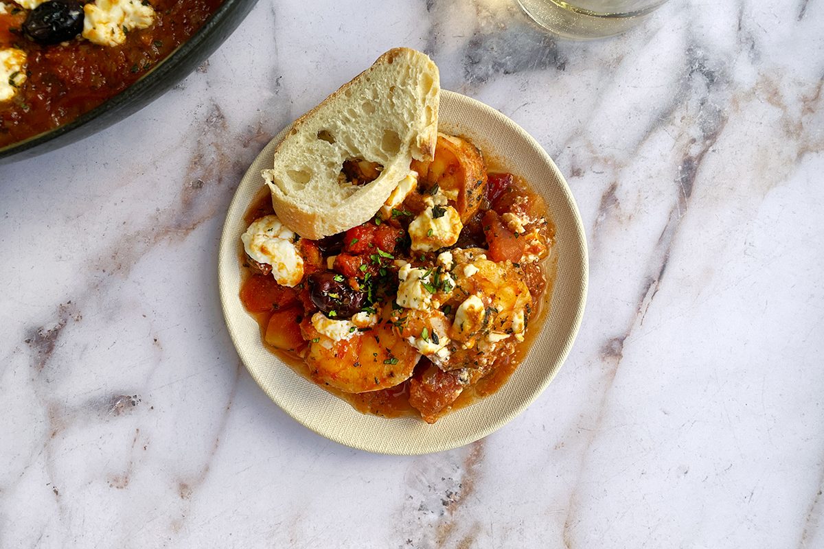 Shrimp saganaki on a small white plate with a slice of baguette.