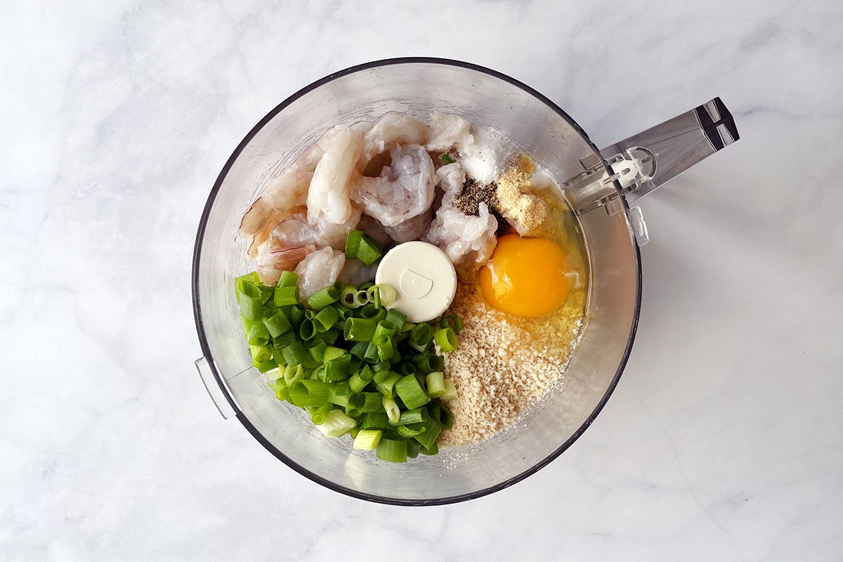 Food processor bowl with ingredients for Taste of Home's shrimp burger: shrimp, panko breadcrumbs, egg, lemon juice, garlic power, green onions, salt, and pepper.