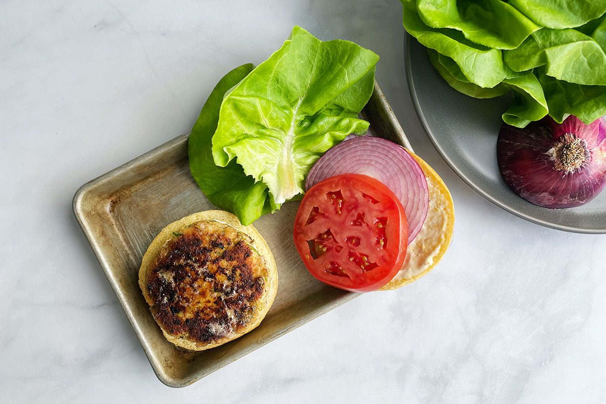 Assembling Taste of Home's shrimp burger patties on buns with lettuce, onion, tomato.