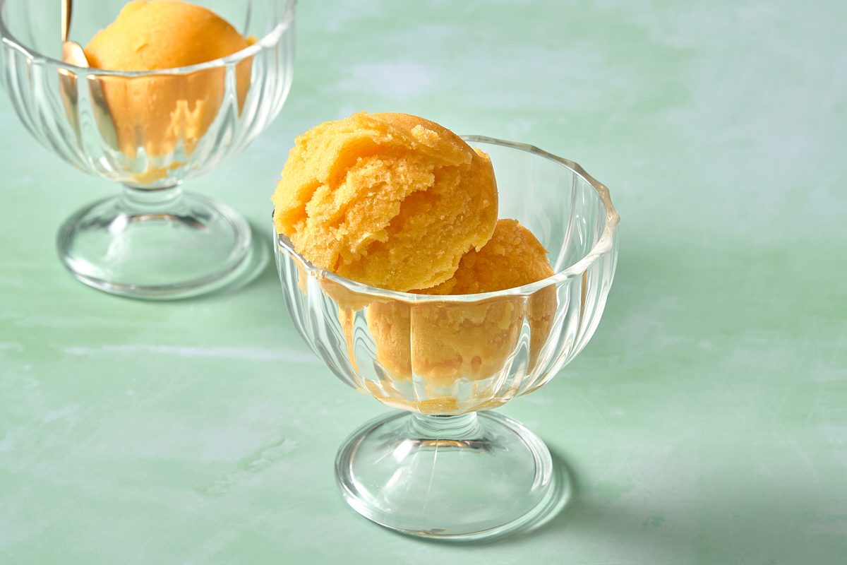 Two scoops of peach sorbet served in a small glass bowl
