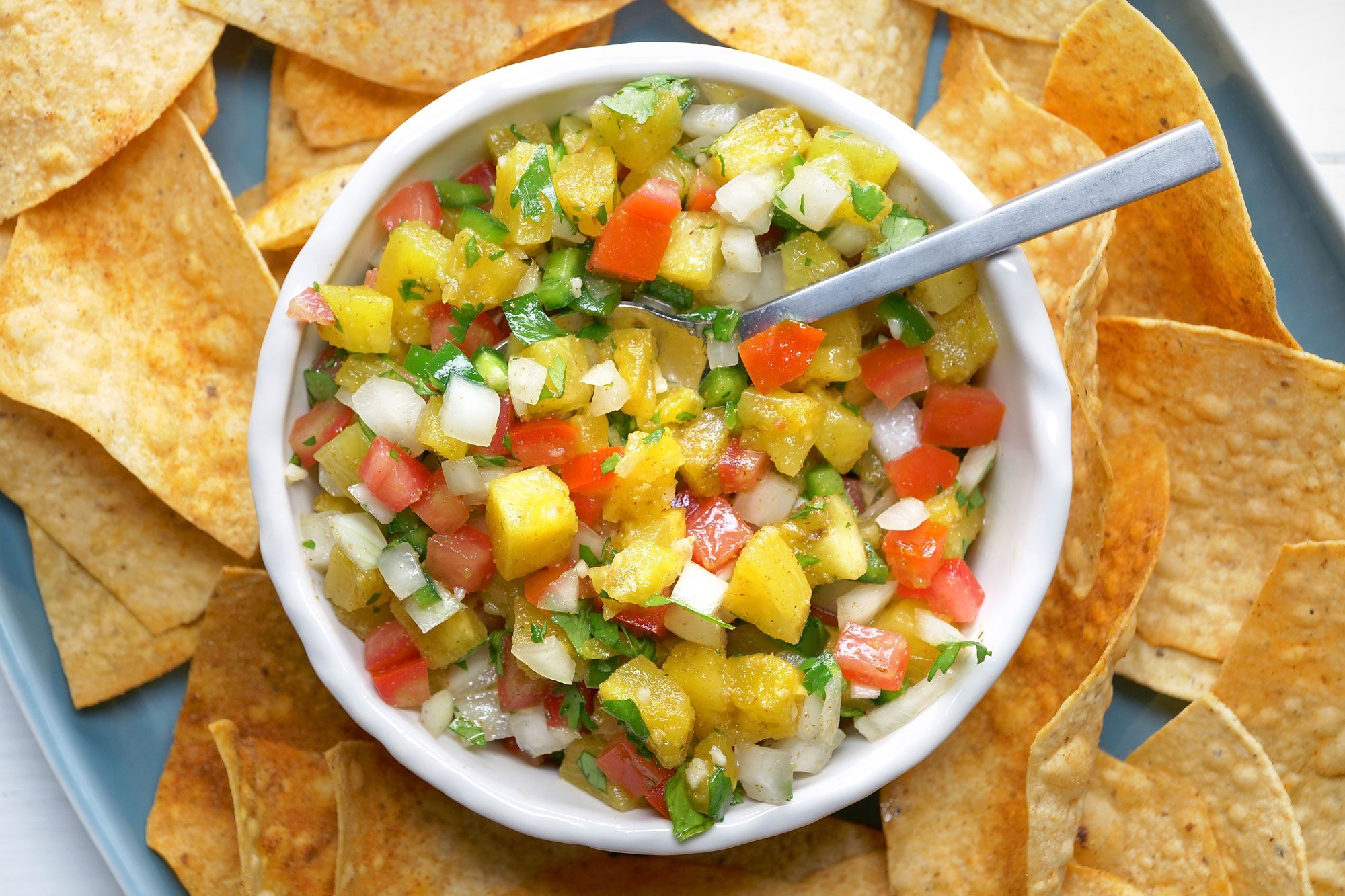overhead shot; white background; Pineapple Salsa in large white bowl served with tortilla chips in a blue plate;