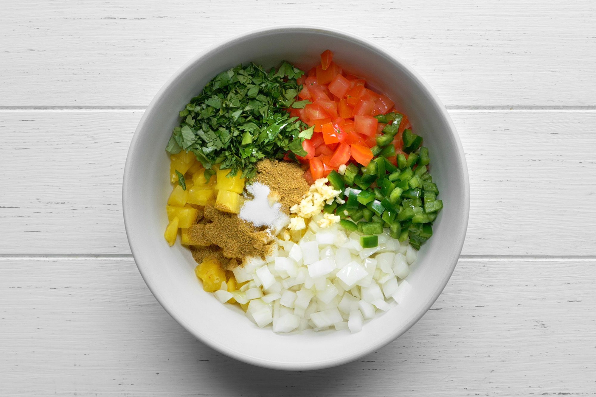 overhead shot; white background; all ingredients for pineapple salsa in a large white bowl;