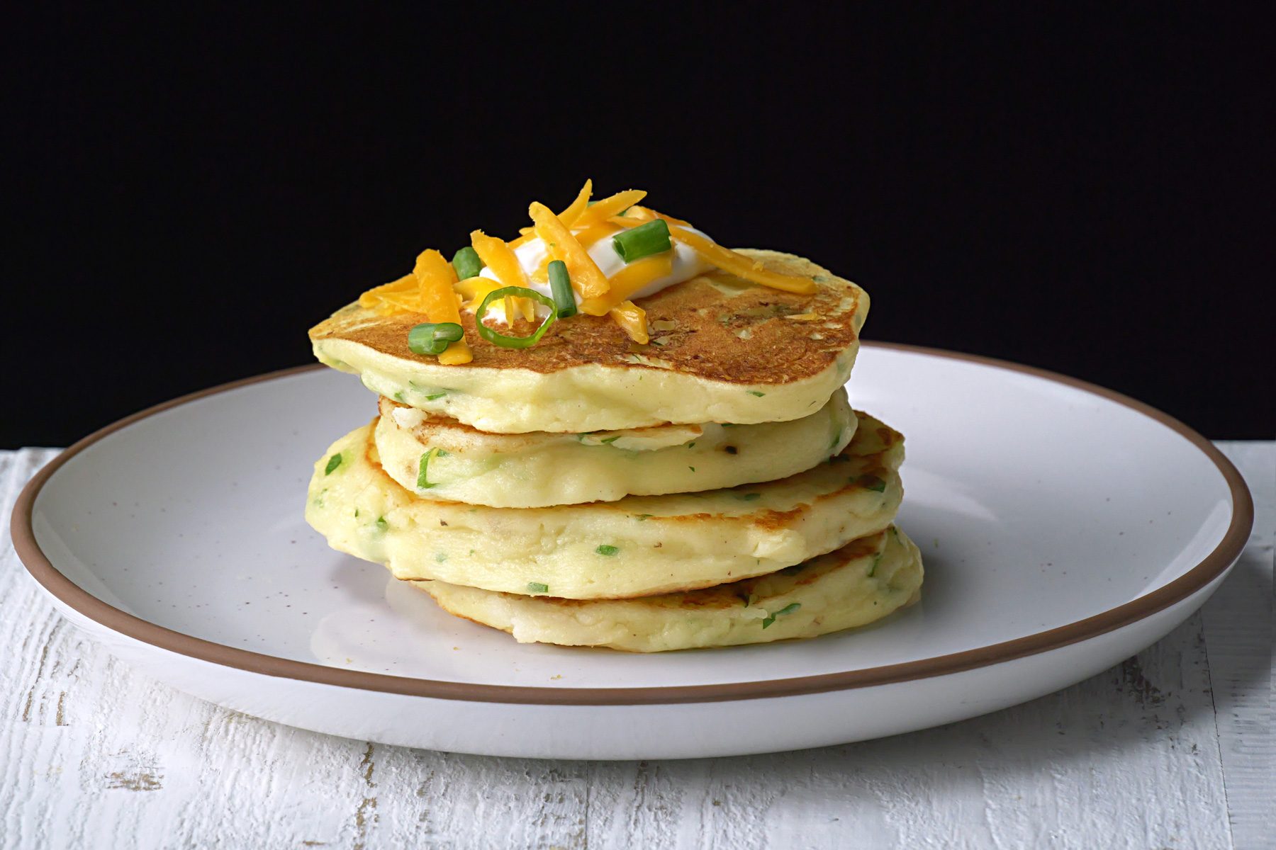 Stack of pancakes with vegetable toppings on a white plate