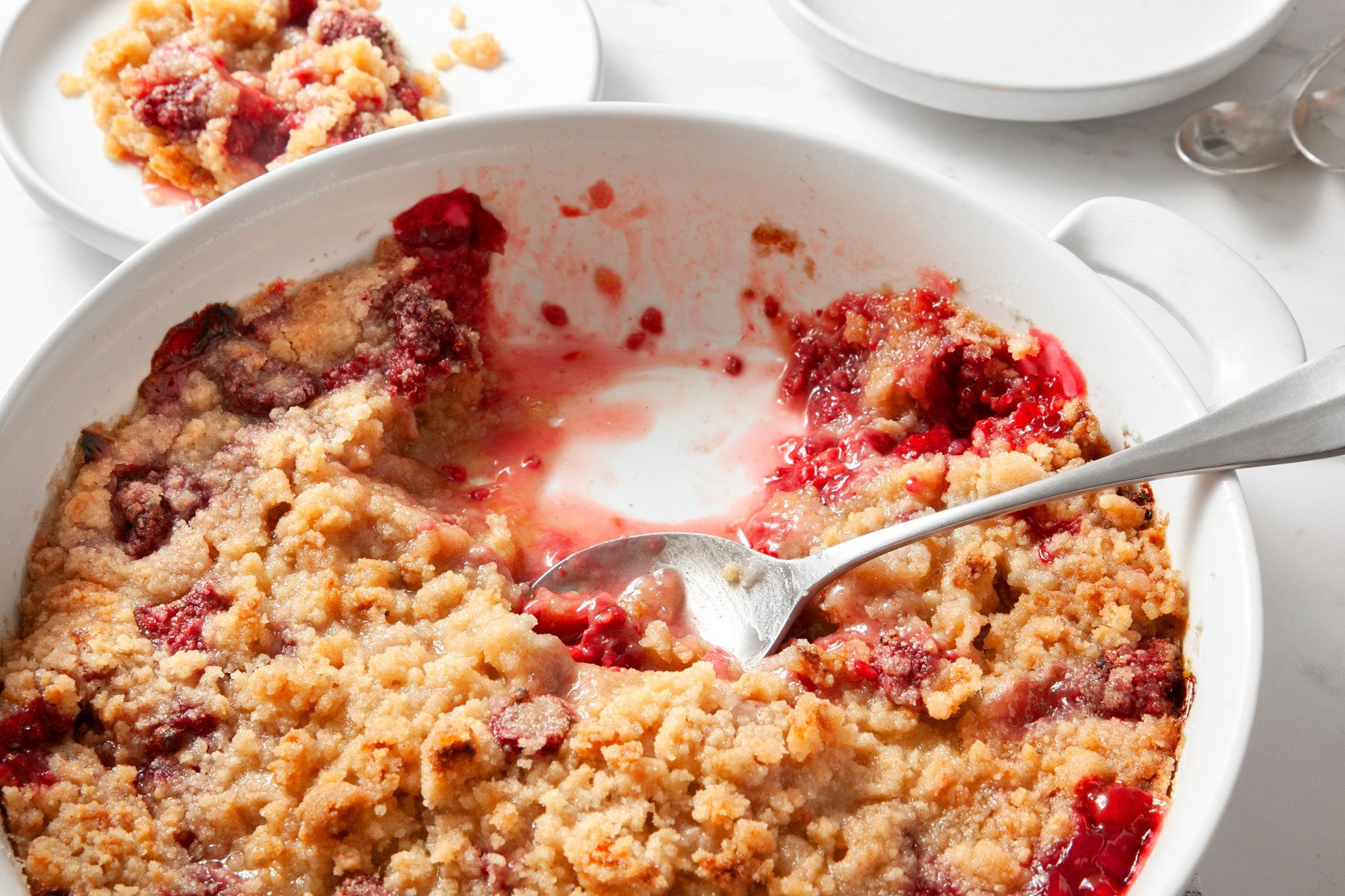 Easy Raspberry Crumble served in a large serving dish over kitchen towel raspberry crumble also served in small plate and one large spoon