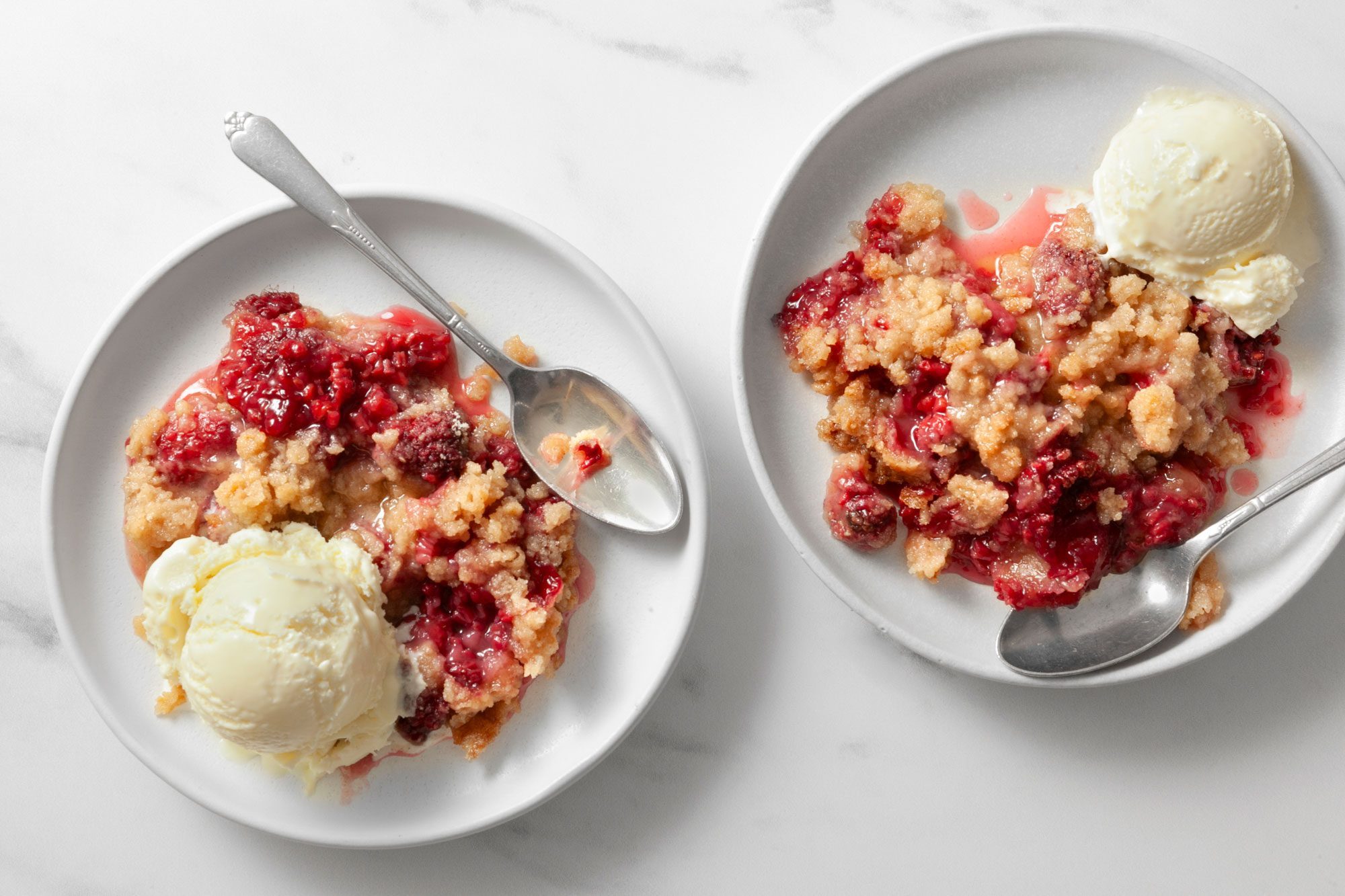 Easy Raspberry Crumble served in two small plates with ice cream scoops and silver spoons