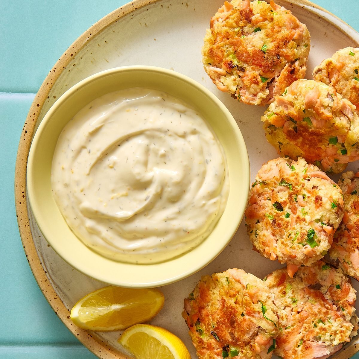 Salmon patty sauce in a bowl with some salmon patties on the side