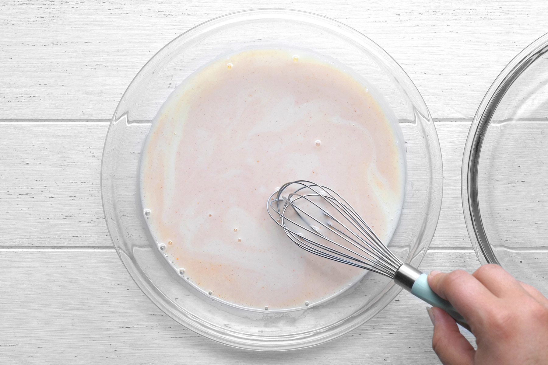 overhead shot; white background; In a shallow bowl, mixing buttermilk and hot sauce