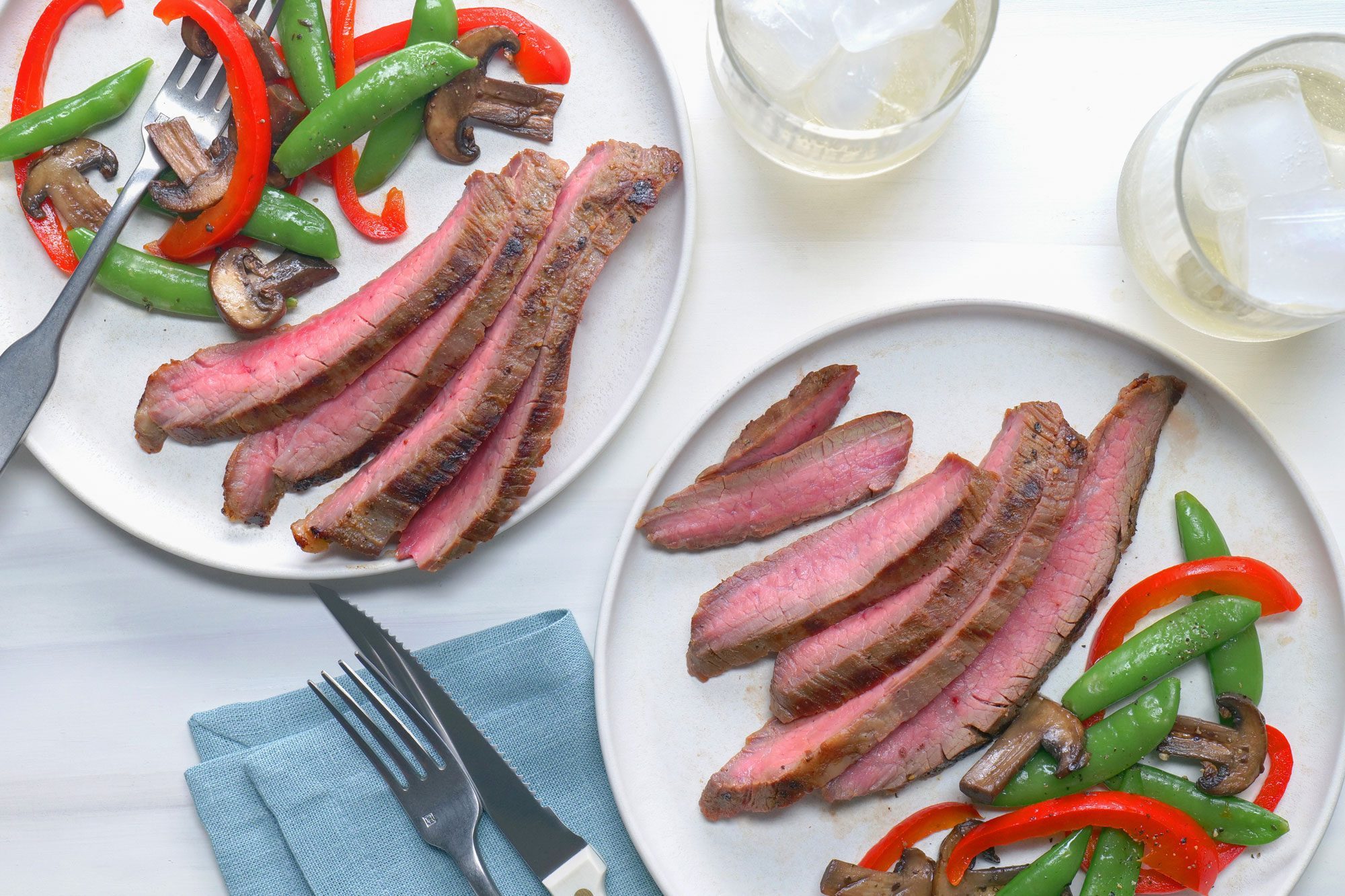 Two plates of Soy Marinated Flank Steak with vegetables elegantly presented on a table