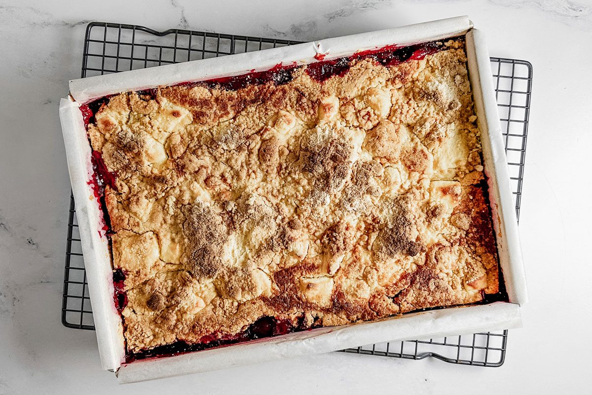 Taste of Home Strawberry Cheesecake Dump Cake in a metal baking pan on a wire cooling rack.