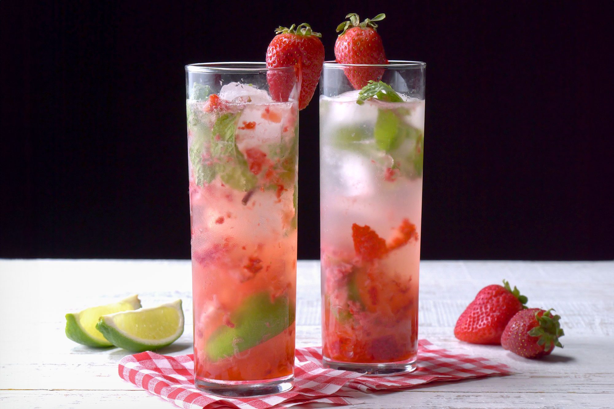 horizontal shot; black background; Strawberry Mojito served in a highball glasses garnished with strawberries placed over kitchen towel;