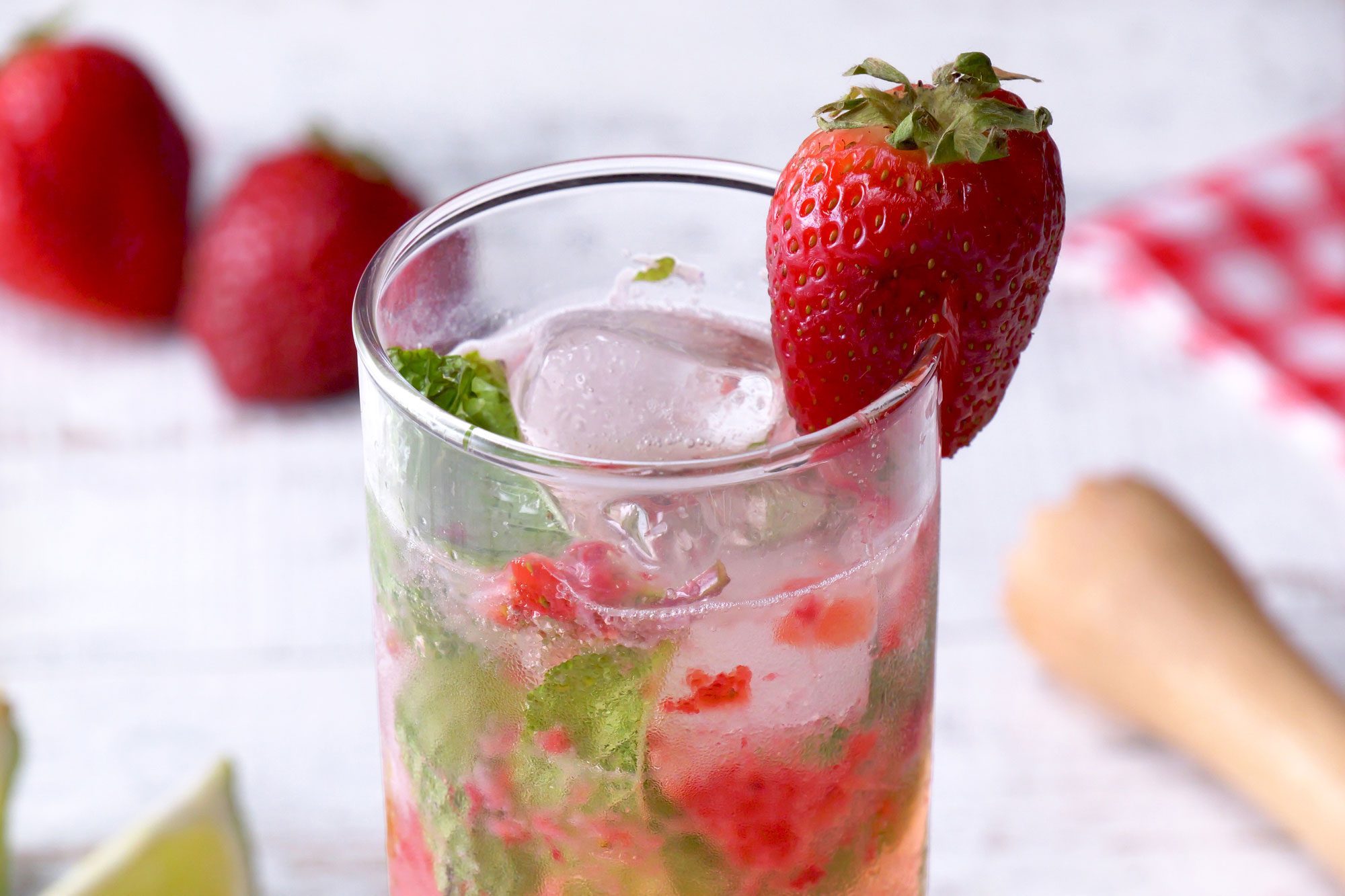 3/4th shot; white background; Strawberry Mojito served in a highball glass garnished with strawberry;