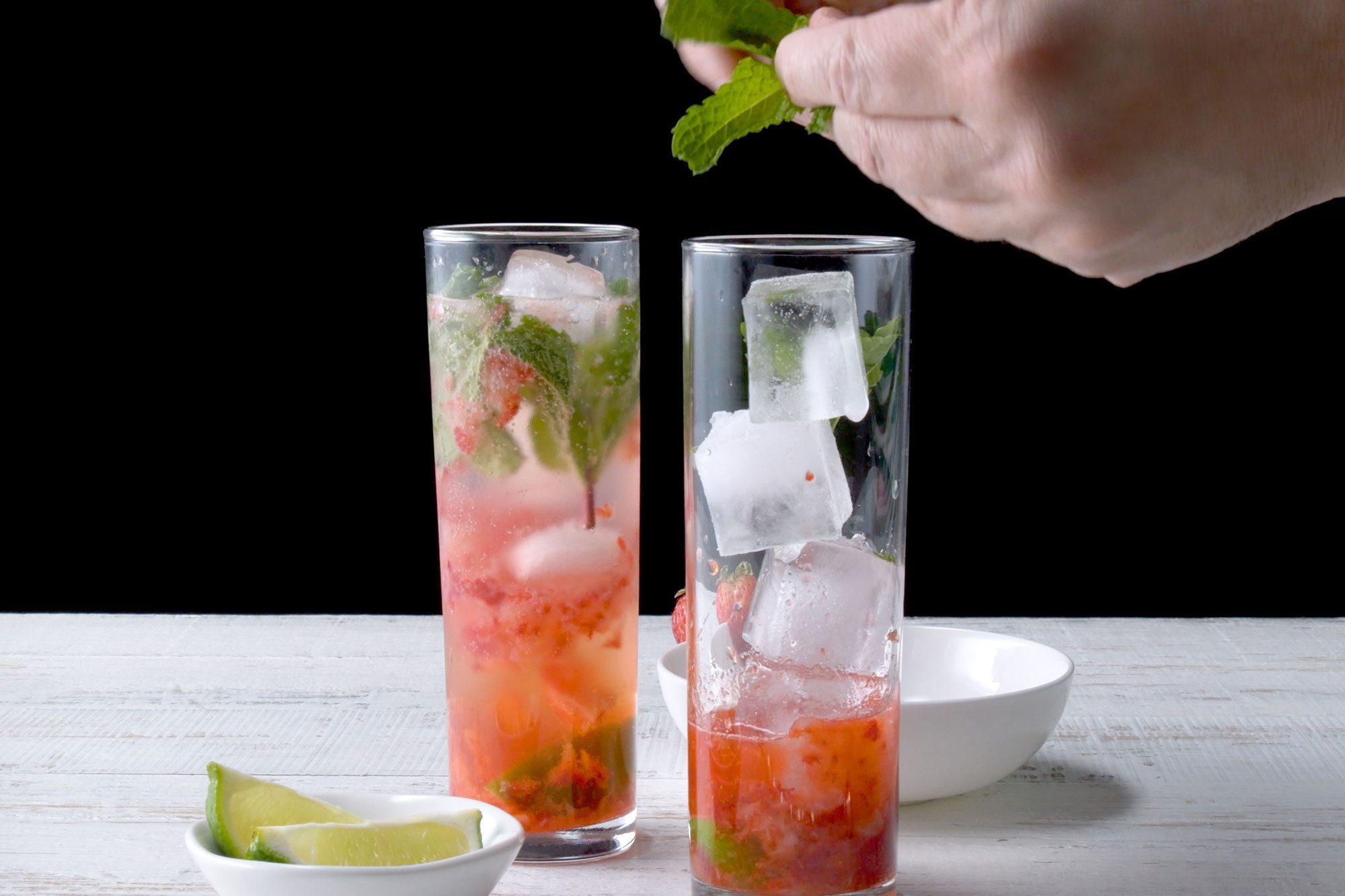 horizontal shot; black background; adding mint in Strawberry Mojito drink;