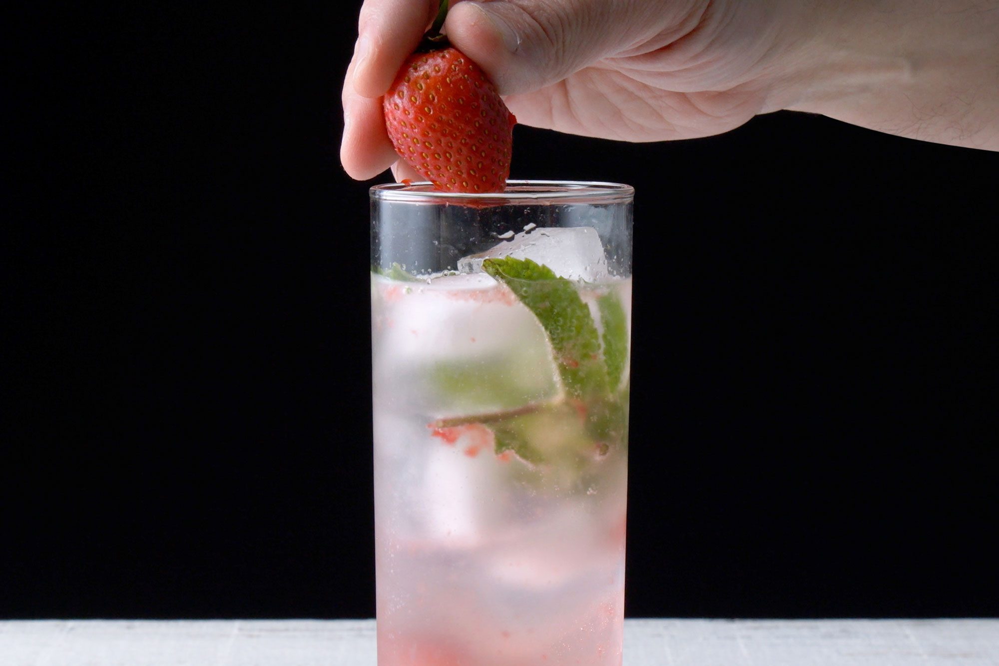 horizontal shot; black background; placing strawberry over glass rim;