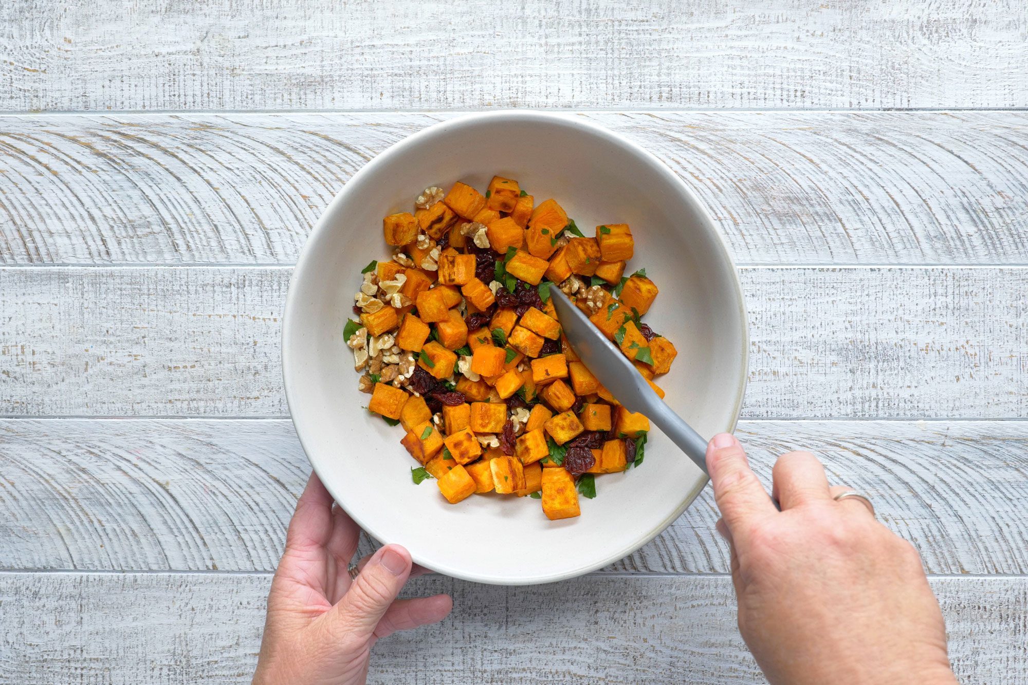 overhead shot of combining the walnuts, cherries, parsley and potatoes in a large bowl; white wooden background;