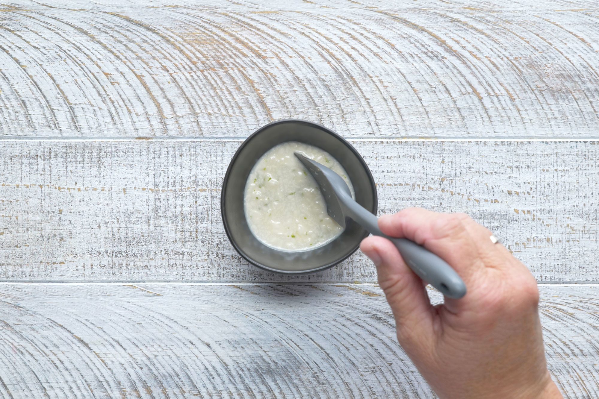 overhead shot of mayonnaise, vinegar, honey, lime zest mix in a small bowl; white wooden background;