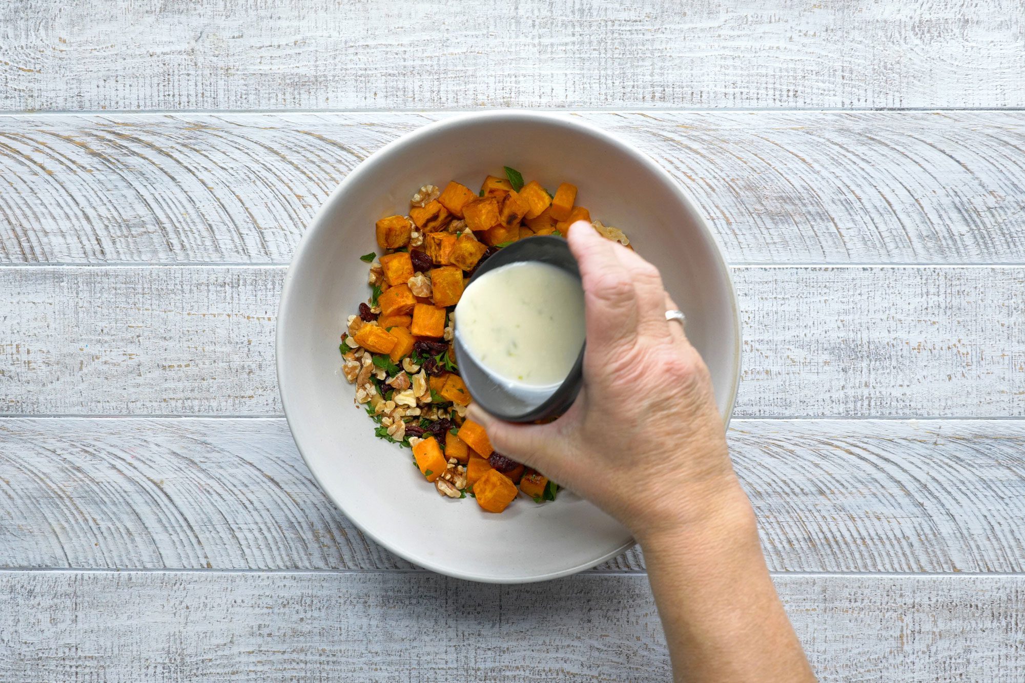 overhead shotof dressing poured over potato mixture; white wooden background;