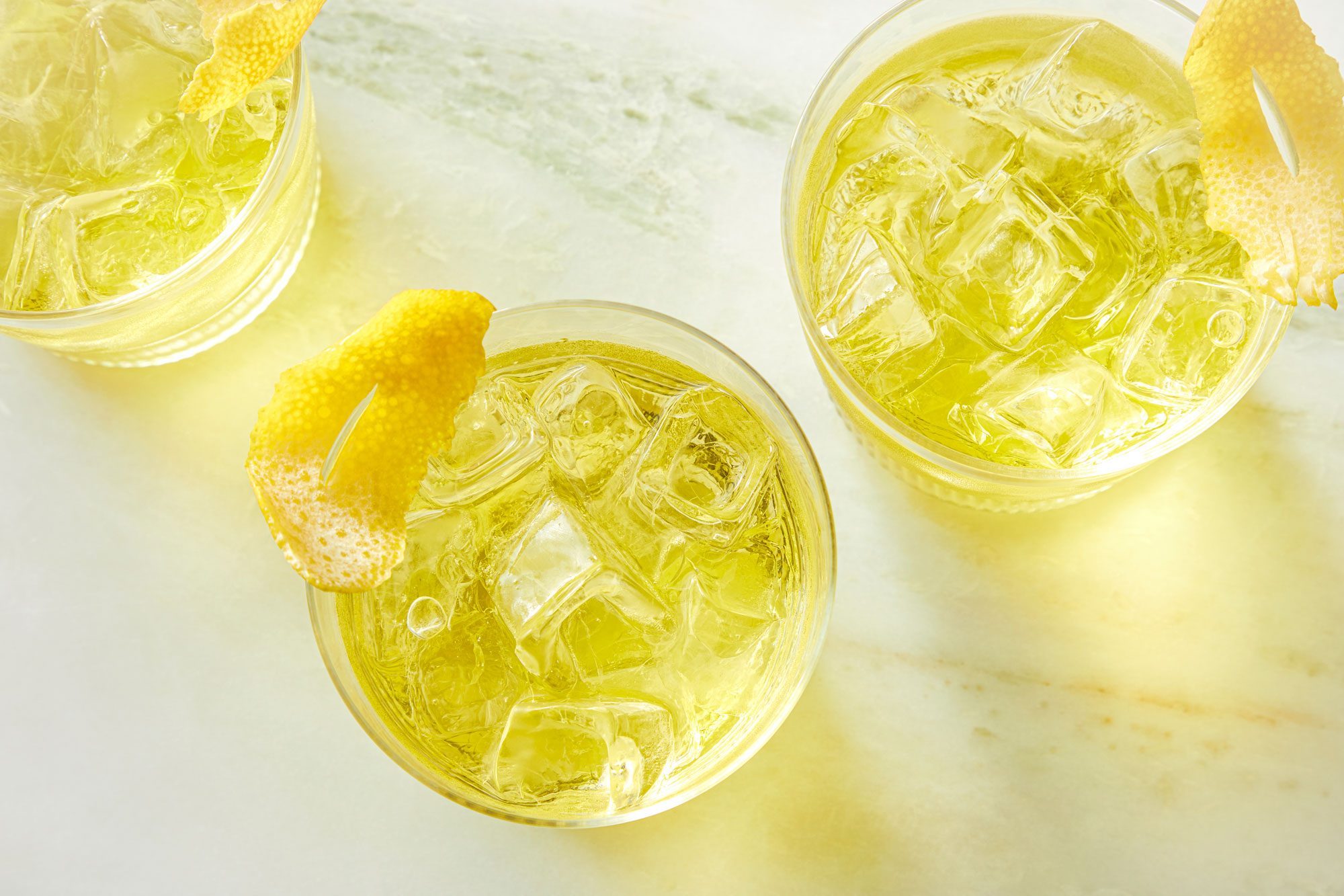 Overhead shot of White Negroni; served in glasses; garnished with lemon peel twist; marble background;