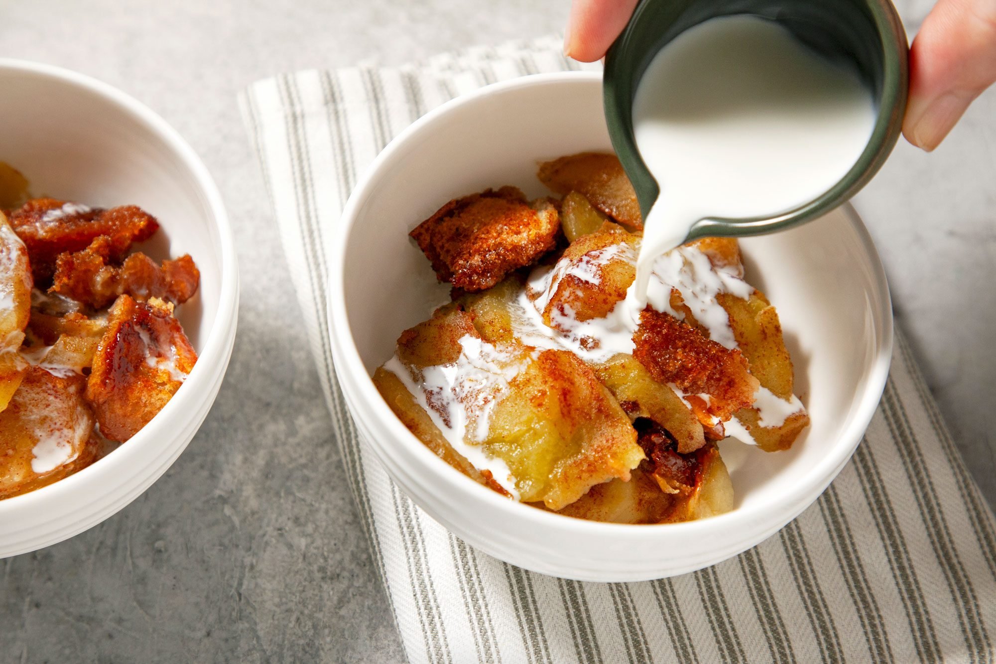 High angle view shot of pour cream over apple brown betty; served warm in two bowls; napkin; grey background;