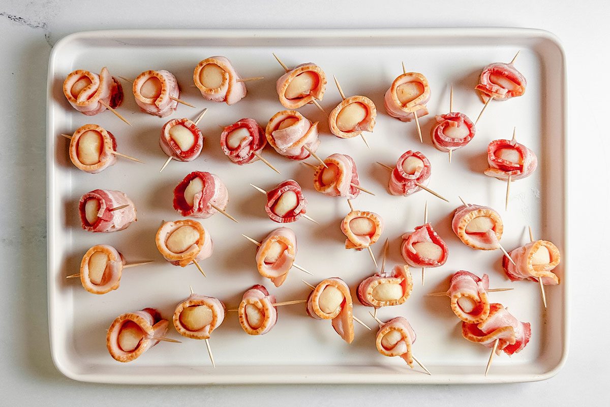 Uncooked Taste of Home bacon wrapped water chestnuts on a white baking sheet.