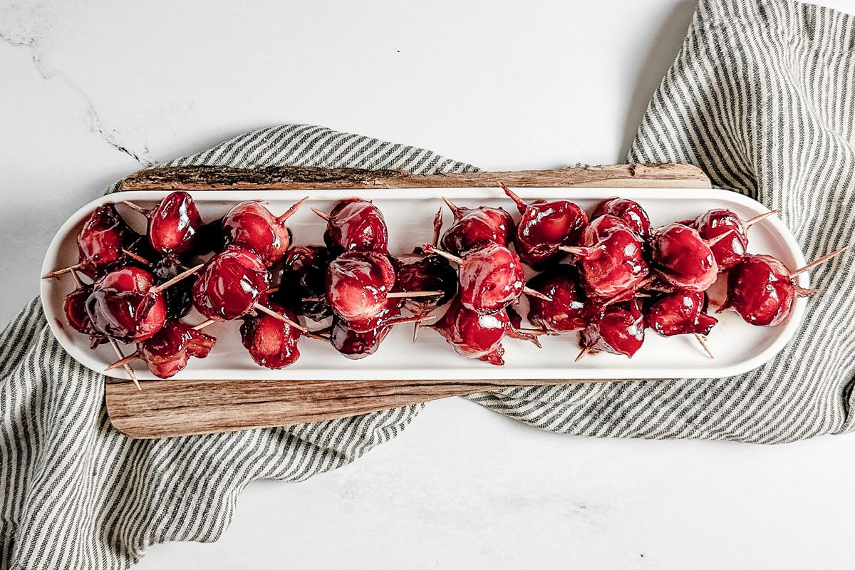 Taste of Home bacon wrapped water chestnuts on a white ceramic tray set on a wooden board atop a striped linen napkin.