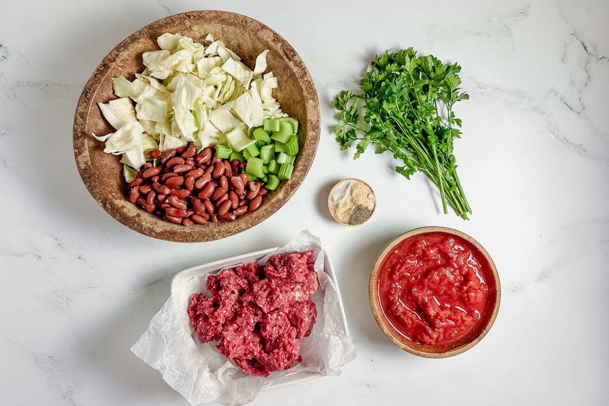 Ingredients for Taste of Home beef cabbage soup in wood and ceramic bowls on a marble surface.