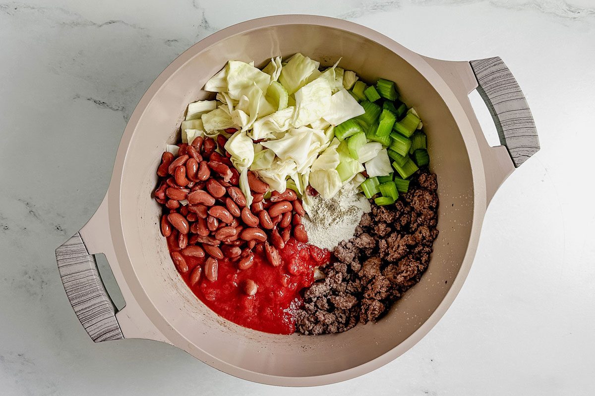 Ingredients for Taste of Home beef cabbage soup in a Dutch oven on a marble surface