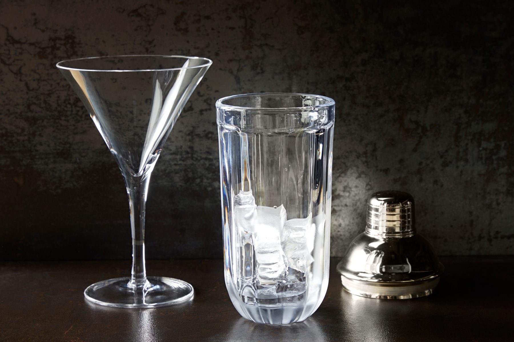 Cocktail glass and shaker with ice half way on a table