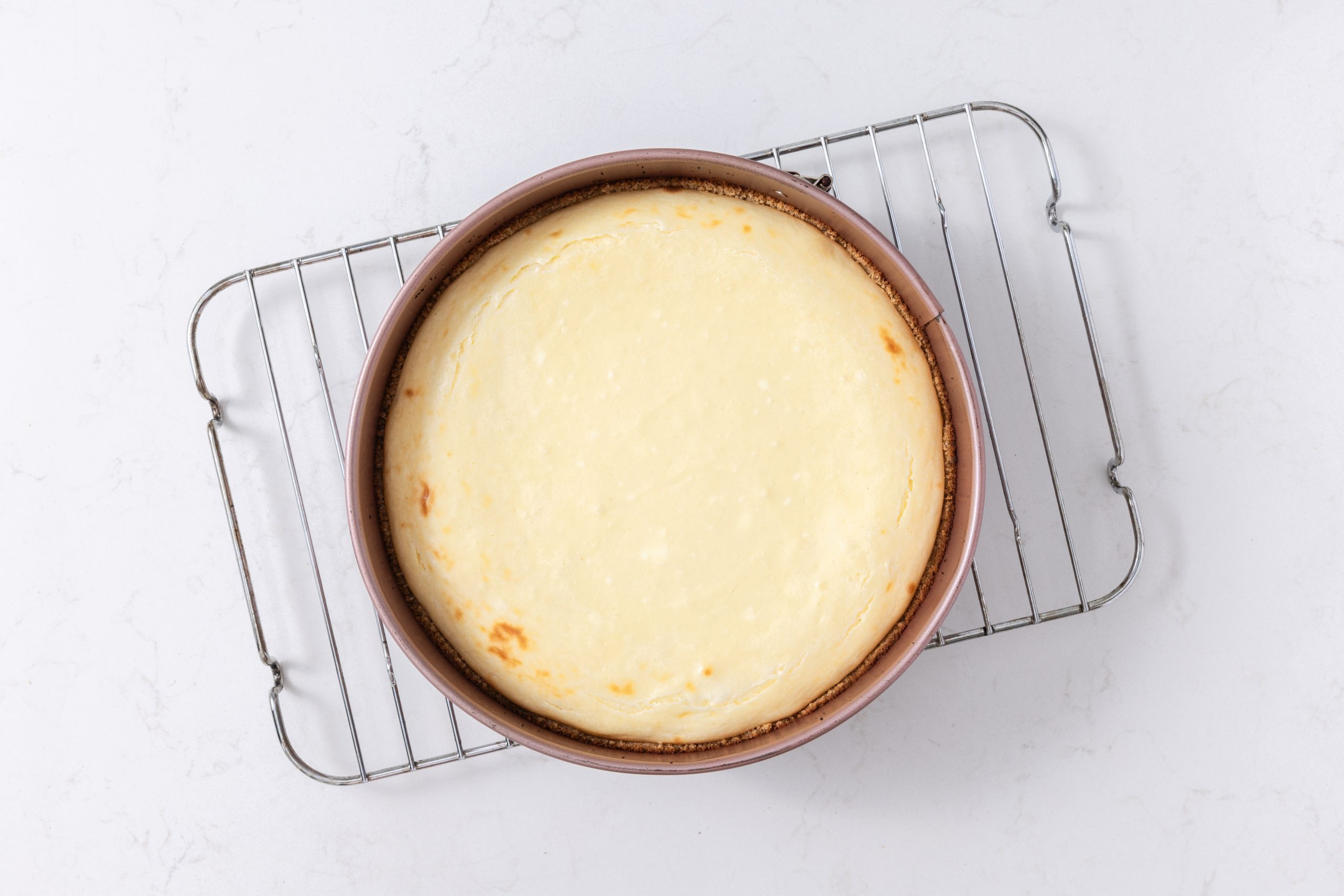 Cheesecake baked and cooling in wire rack.